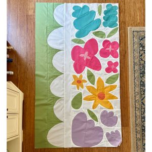 row of colorful flower quilt blocks made with solid color fabric and a curvy green border on the floor