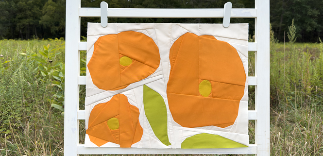 abstract flower quilt block on a white background hanging on a fence in a field outdoors