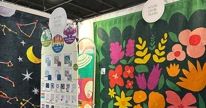 detail of Whole Circle Studio booth at h+h americas 2026 with modern quilts, quilt patterns, and embroidery designs.