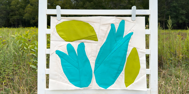 abstract blue flower quilt block on a white background hanging on a fence in a field outdoors