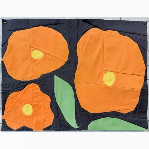 3 abstract orange flowers and 2 green leaves quilt block on a navy background