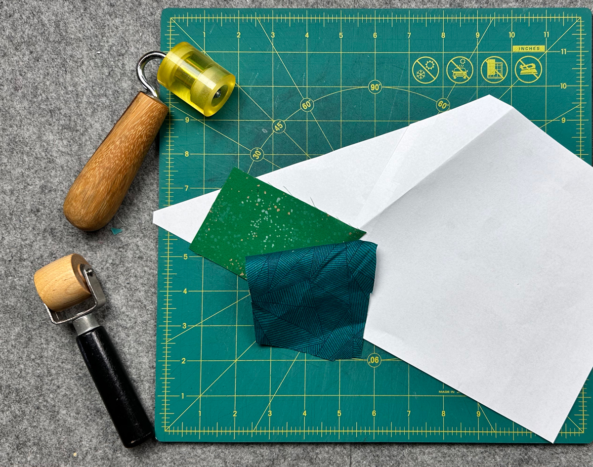 A partially completed foundation paper pieced quilt section rests on a cutting mat beside seam rollers