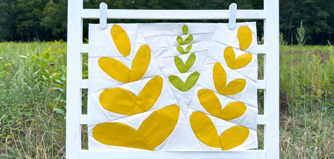 abstract flower quilt block on a white background hanging on a fence in a field outdoors