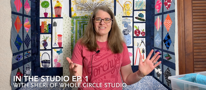 smiling woman talking with her hands up in front of a scrappy quilt