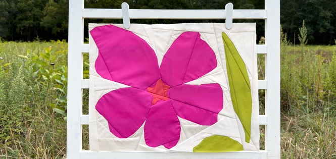 abstract magneta hibiscus quilt block on a white background hanging on a fence in a field outdoors