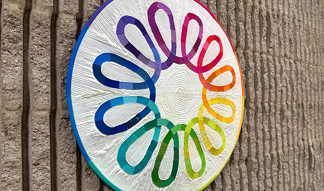 detail of colorful fiber art with 12 loops arranged in a circle hanging on a concrete wall